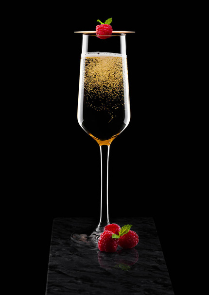 Elegant glas gele Champagne met rasspbery en verse bessen met mint blad op stok op zwarte marmeren bord op zwarte achtergrond.  - Foto, afbeelding