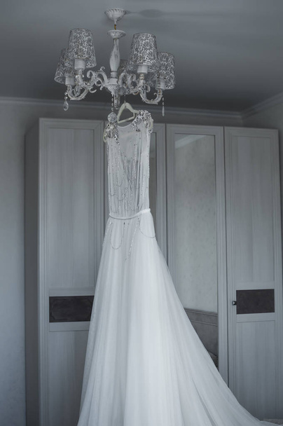 the bride's wedding dress hangs on the chandelier. wedding. selective focus. film grain. - Fotó, kép
