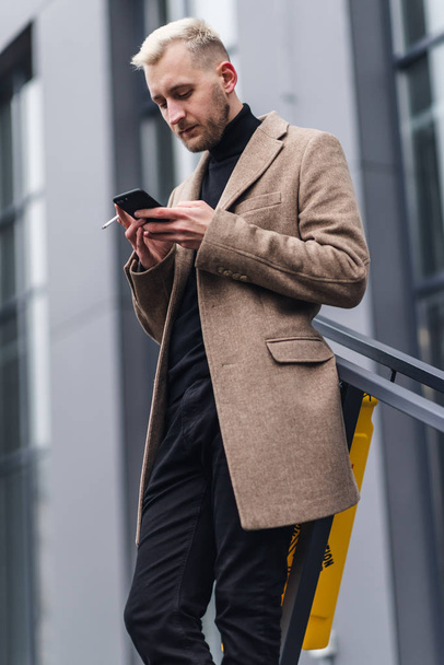 Young Attractive Businessman Standing near Big Modern Office Building. Typing a Message on his Smartphone. - Photo, image