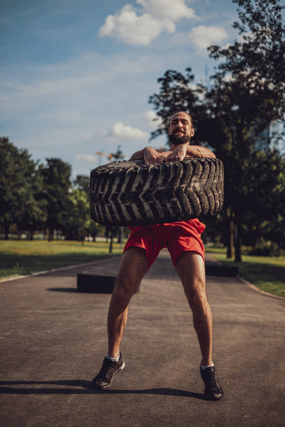 Bearded athlete trying to lift tire in the park - Foto, afbeelding