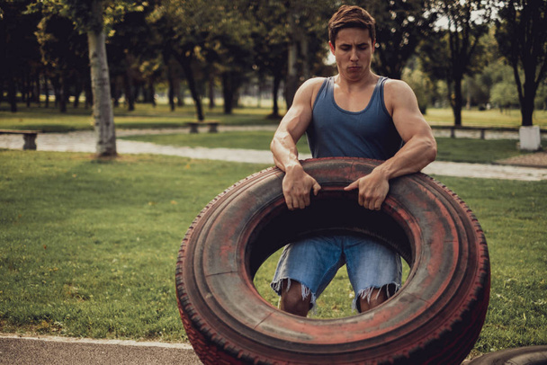 Athletic man training with tire in the park - Photo, Image