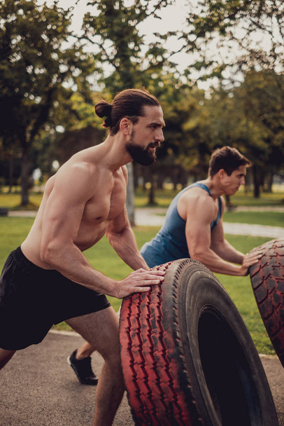 Robuste muskulöse Männer, die im Park Reifen umdrehen - Foto, Bild