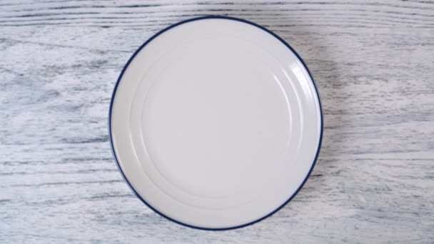White plate with a blue stripe on the edge. Top view on a white wooden background - 映像、動画