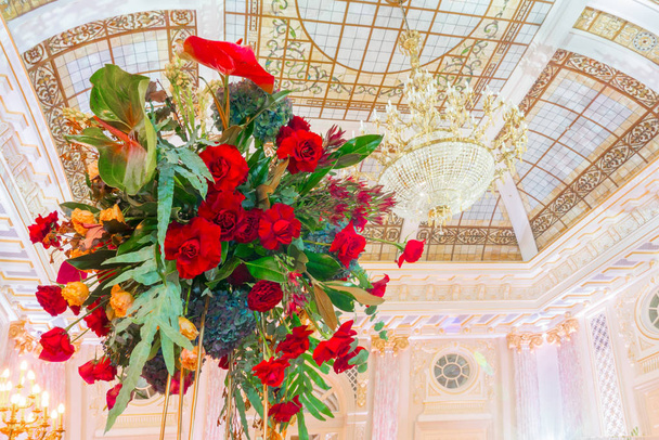 Μπουκέτα με λουλούδια που κρέμονται από το ταβάνι. Κόκκινα τριαντάφυλλα σε μπουγκέ με εξωτικά λουλούδια. Υπέροχος πολυέλαιος στο ταβάνι. Εσωτερικό παλάτι. Μουσείο Παλατιού. Κλάση Lux. - Φωτογραφία, εικόνα