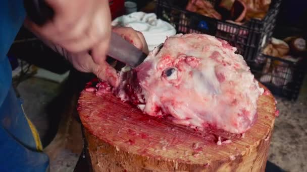 Macro vista de un trabajador cortando con un cuchillo grande la carne exterior del cráneo de un cerdo en un tronco de madera
 - Metraje, vídeo