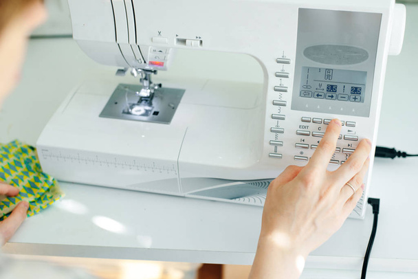 Las manos femeninas que cosen la tela blanca en la máquina de fabricación profesional en el lugar de trabajo
 - Foto, imagen