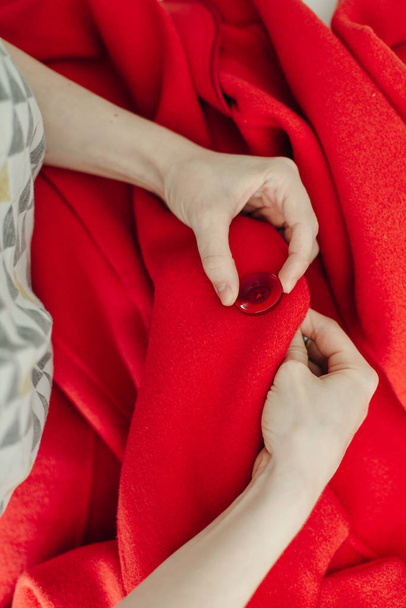 швачка пришиває кнопку на червоному пальто на білому столі
 - Фото, зображення