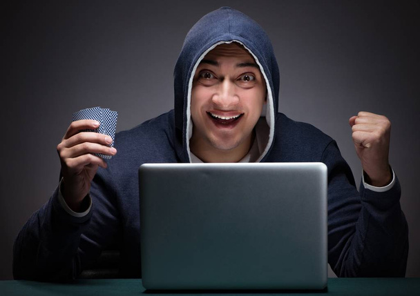 Giovane uomo che indossa una felpa con cappuccio seduto davanti a un computer portatile - Foto, immagini