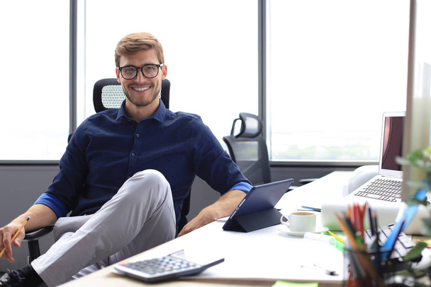 Young modern business man working using digital tablet while sitting in the office. - Foto, Bild