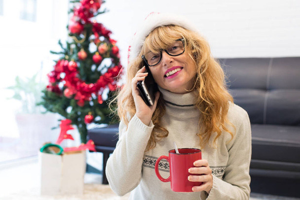 mujer adulta con sombrero de Navidad y teléfono móvil en casa
 - Foto, imagen