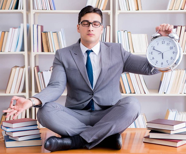 Businessman student in lotus position with an alarm clock in lib - Photo, Image