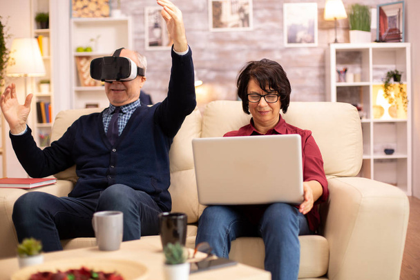 Old elderly retired man using VR virtual reality headset in their cozy apartment - Foto, Imagen