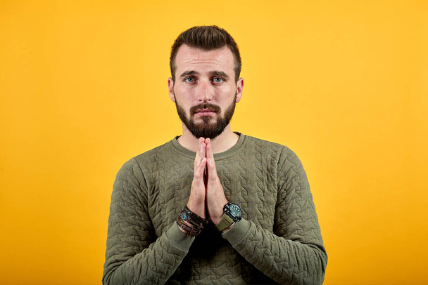 Peaceful handsome man keeping hands together, praying, looking at camera - Foto, imagen