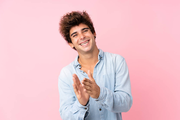 Giovane uomo caucasico con camicia jeans su sfondo rosa isolato applaudendo dopo la presentazione in una conferenza
 - Foto, immagini