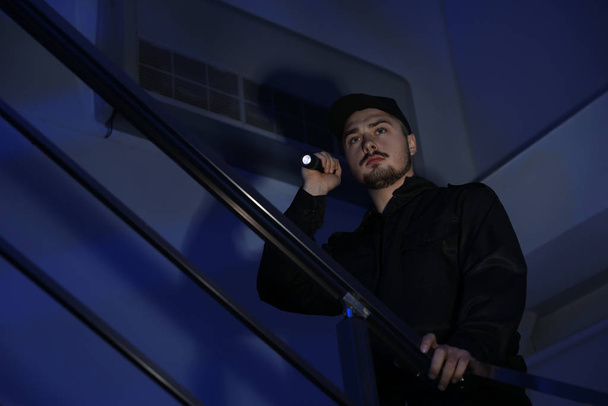 Male security guard with flashlight on stairs in darkness - Фото, зображення