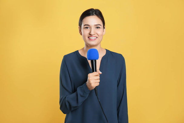 Young female journalist with microphone on yellow background - Foto, Bild