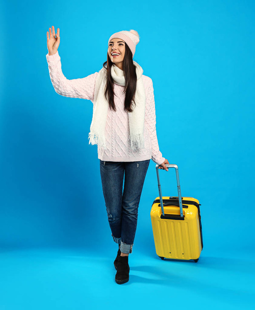 Young woman in warm clothes with suitcase on blue background. Winter vacation - Fotó, kép