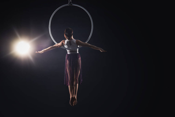 Young woman performing acrobatic element on aerial ring against  - 写真・画像
