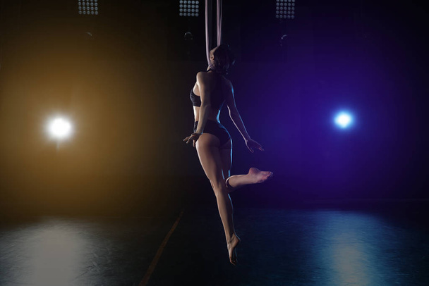 Young woman performing acrobatic element on aerial silk indoors - Foto, afbeelding
