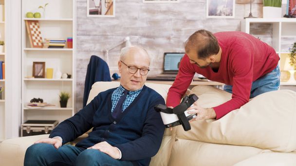 Племянник показывает дедушке, как пользоваться VR гарнитурой.
 - Фото, изображение