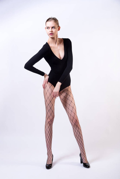 Fashion portrait of woman in  studio. High young model girl in  stylish clothes, in pantyhose nets and high heels posing in studio, portrait of beautiful woman, model posing training - 写真・画像