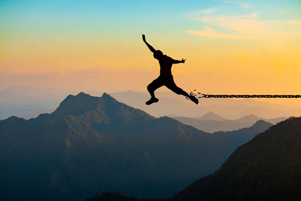 Concepto de libertad, silueta de un hombre saltando y cadenas rotas en la montaña con cielo al atardecer
. - Foto, Imagen