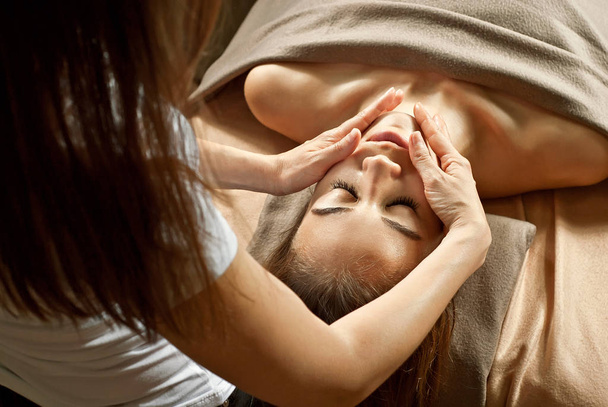 Meisje doet gezichtsmassage. Handen van masseur close-up. naakt brunette bedekt met handdoek. - Foto, afbeelding