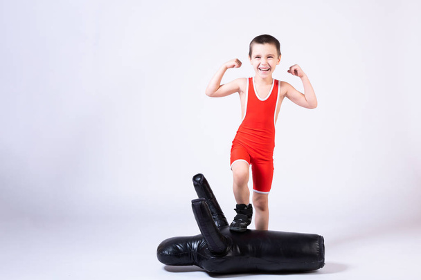 Cheerful sports boy in wrestling tights and wrestling shows biceps, rejoices in victory, stands over a defeated sports dummy for training and handling techniques from various martial arts on a fir-tree isolated background.  - Foto, Imagem