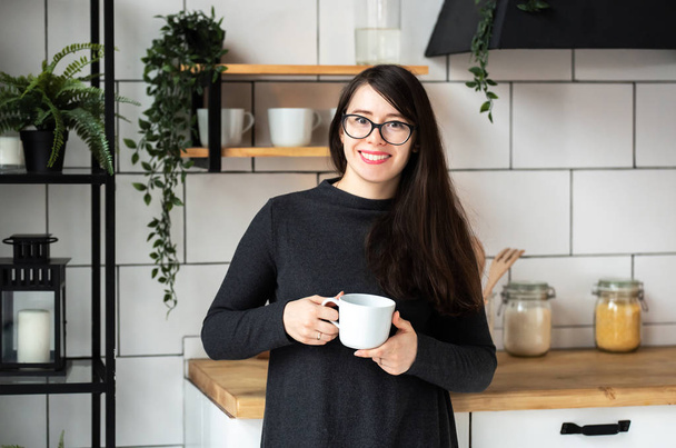 Young woman in a dark gray dress in the modern kitchen, the kitchen drinking tea. - Fotoğraf, Görsel