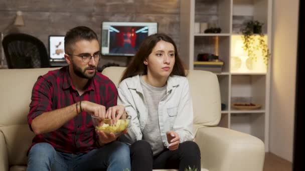 Caucásico joven pareja comiendo patatas fritas mientras viendo la televisión
 - Metraje, vídeo