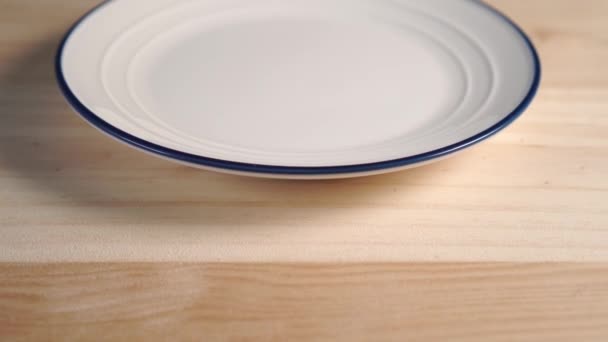 Nahaufnahme eines weißen Tellers mit einem blauen Streifen am Rand. auf einem hölzernen Hintergrund. Kameraspur - Filmmaterial, Video