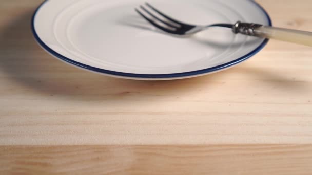 ein weißer Teller mit blauem Streifen am Rand einer Nahaufnahme mit einer Dessertgabel. auf einem hölzernen Hintergrund. Kameraspur - Filmmaterial, Video