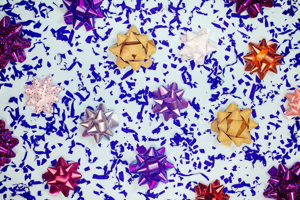 Gift bows and confetti festive bright background. Colorful present ribbon knots with blue paper pieces holiday composition. Christmas, birthday decorative colorful backdrop for greeting card. - Φωτογραφία, εικόνα