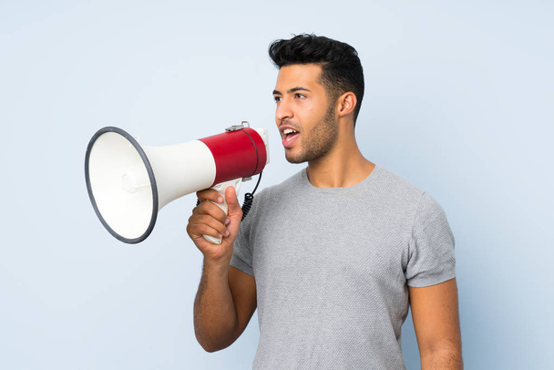 Young handsome man over isolated background shouting through a megaphone - Photo, Image