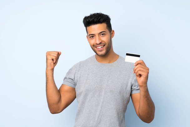 Young handsome man over isolated background holding a credit card - Foto, afbeelding