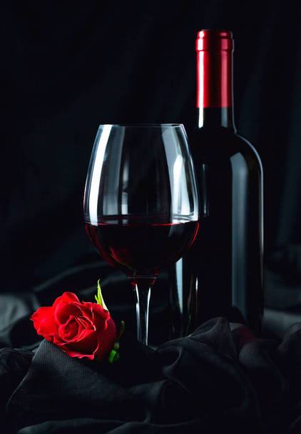 Κόκκινο κρασί και κόκκινο τριαντάφυλλο σε μαύρο φόντο. - Φωτογραφία, εικόνα