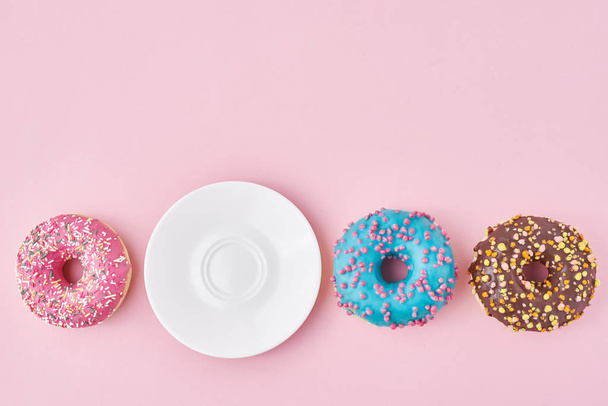 Різні барвисті пончики і порожня тарілка на рожевому фоні. концепція креативної їжі
 - Фото, зображення