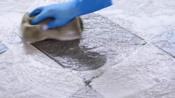 Hand of man met blauwe rubberen handschoenen gebruikt een spons om de tegelvloer schoon te maken. - Video