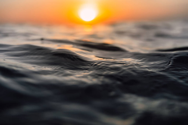 Zonsondergang en golven in de oceaan. Warme water textuur met bokeh - Foto, afbeelding