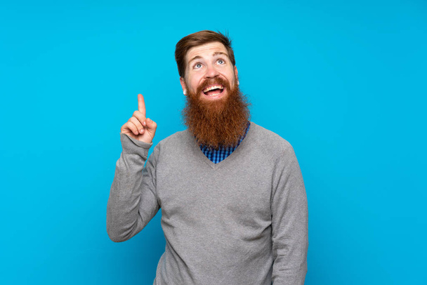 Homme rousse à longue barbe sur fond bleu isolé pointant vers le haut et surpris
 - Photo, image