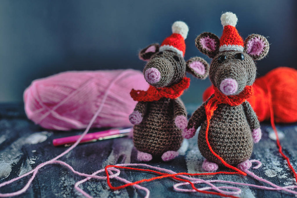 Krásné ručně vyrobené amigurumi krysy s vánočními klobouky a červenými šátky stojící v blízkosti jasné příze kreslí na modrém pozadí. Nový rok 2020 koncept - Fotografie, Obrázek