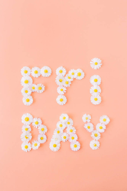 Word FRIDAY made of chamomile daisy buds on coral peach background. Flat lay, top view minimal creative floral composition. - Photo, Image