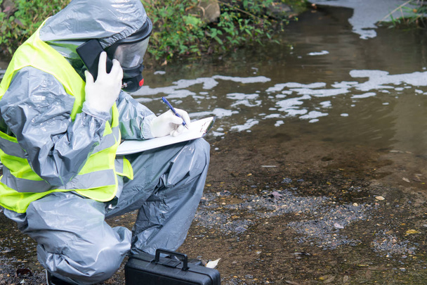 specialist in a protective suit and mask, on the pond, calls the mobile phone management, to report the results of the study, close-up - Foto, Imagem