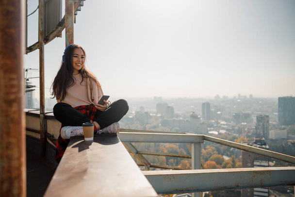 Pretty smiling girl sitting with hot drink on the roof - Фото, изображение