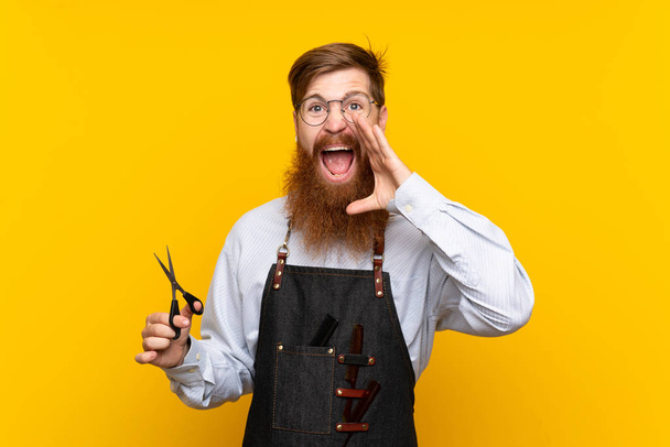 Барбер з довгою бородою в фартусі над ізольованим жовтим фоном кричить з відкритим ротом - Фото, зображення