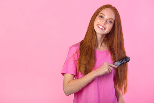 beautiful young woman with red hair on a pink background with a comb - Foto, Imagen