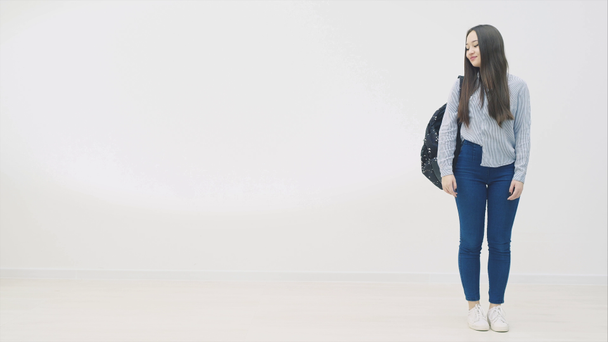 Bella sorridente asiatica giovane adolescente studentessa del liceo indossa jeans e camicia di jeans blu, zaino della scuola sopra la spalla. Guardando di lato, annuendo con la testa, alzando il pollice
. - Filmati, video