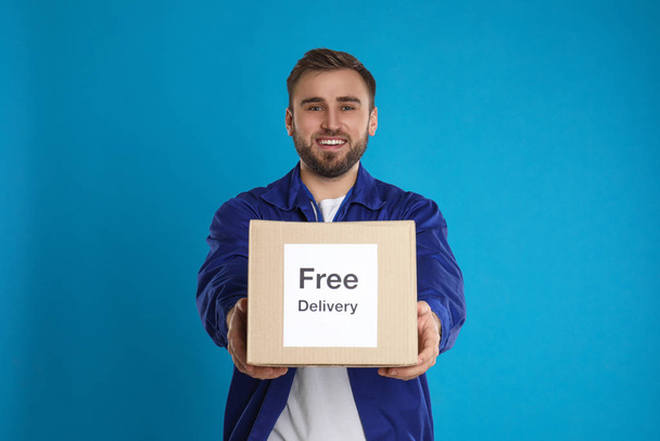 Male courier holding parcel with sticker Free Delivery on light blue background - 写真・画像
