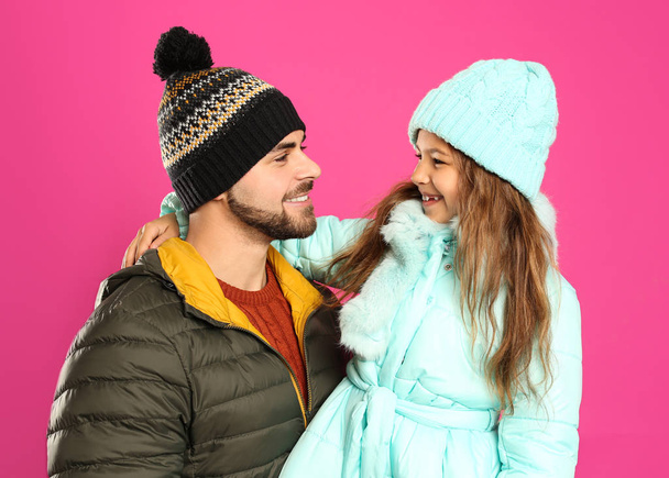 Happy father and daughter in warm clothes on pink background. Winter vacation - Zdjęcie, obraz