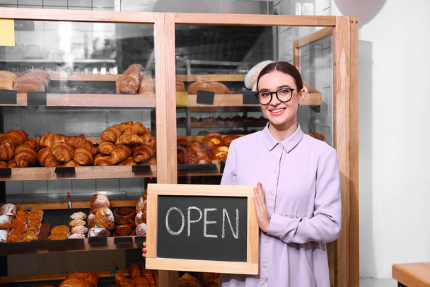 Female business owner holding OPEN sign in bakery - Фото, изображение